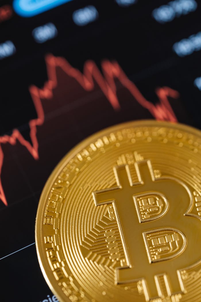 Close-up of a gold Bitcoin coin with a fluctuating stock market graph in the background.